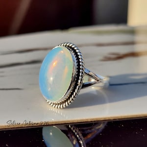 May include: A silver ring with an oval-shaped opal gemstone. The ring has a rope-like design around the stone.
