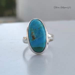 May include: A silver ring with a large oval turquoise stone. The stone has a blue and green color with brown markings.