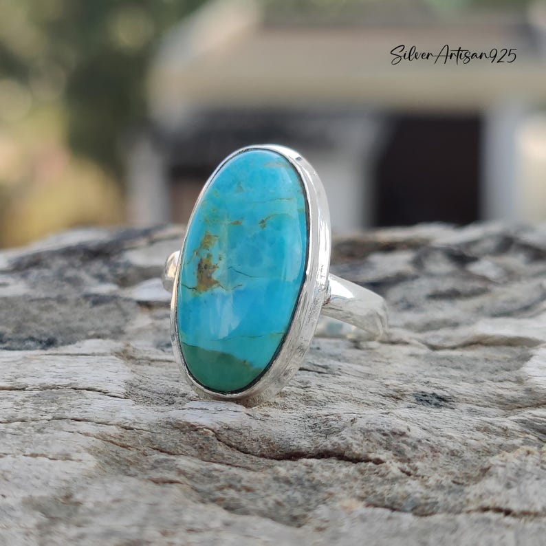 May include: A silver ring with a large oval turquoise stone set in a bezel setting. The stone is a vibrant blue-green color with brown matrix.