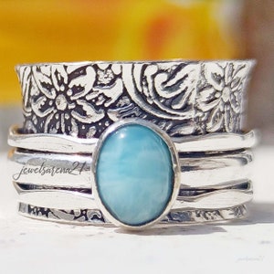 May include: A silver ring with a blue gemstone and a floral design. The ring is made of multiple bands and has a textured finish.