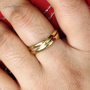 May include: A gold-colored ring with a twisted design, worn on a finger. The ring has a smooth, polished surface and reflects light. The background is a red fabric. The text "SilverArtisan925" is in the upper left corner.