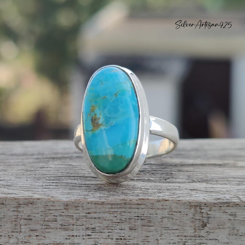 May include: A silver ring with a large oval turquoise stone set in a bezel setting. The stone is a vibrant blue with brown and green inclusions.