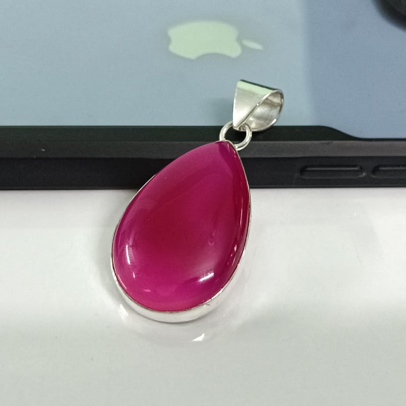 May include: A teardrop-shaped pendant with a bright pink gemstone set in a silver frame.