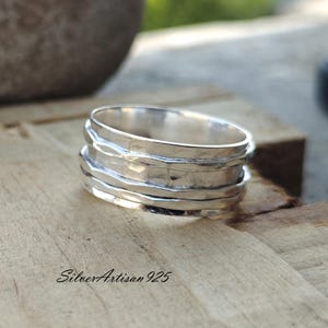 May include: A silver spinning ring with a hammered texture. The ring is made of sterling silver and has a simple, modern design.