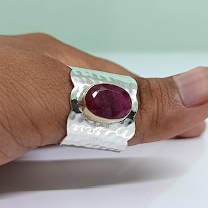 May include: A silver ring with a hammered texture and a large oval ruby gemstone set in the centre.