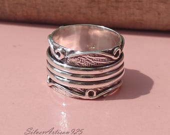 May include: A silver ring with a textured design of leaves and swirls. The ring is made of multiple bands that spin around each other.