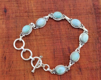 May include: A silver bracelet with a toggle clasp features oval-shaped turquoise stones set in silver.
