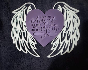 May include: A decorative piece featuring a purple heart with the text "I have an Angel in Heaven and I call her Mom" surrounded by white angel wings. The wings have a detailed, open design.
