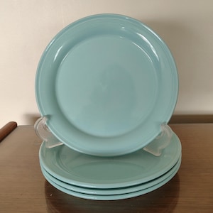 May include: A stack of four turquoise ceramic plates. The plates are round with a slightly raised rim and a smooth, glossy finish. The plates are stacked on top of each other, with the top plate angled slightly upward.