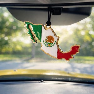May include: Wooden car air freshener shaped like the map of Mexico, featuring the Mexican flag's colors: green, white, and red. The center displays the Mexican coat of arms. It hangs from a black string, suspended from a car's rearview mirror.