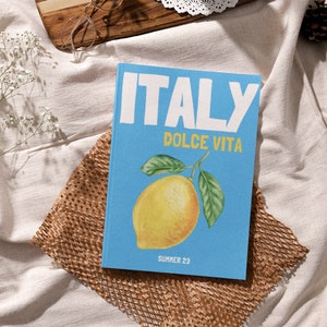 Puede incluir: Un libro azul con el texto "ITALY DOLCE VITA" y una ilustraci&oacute;n de lim&oacute;n. El texto "SUMMER 23" est&aacute; en la parte inferior del libro.