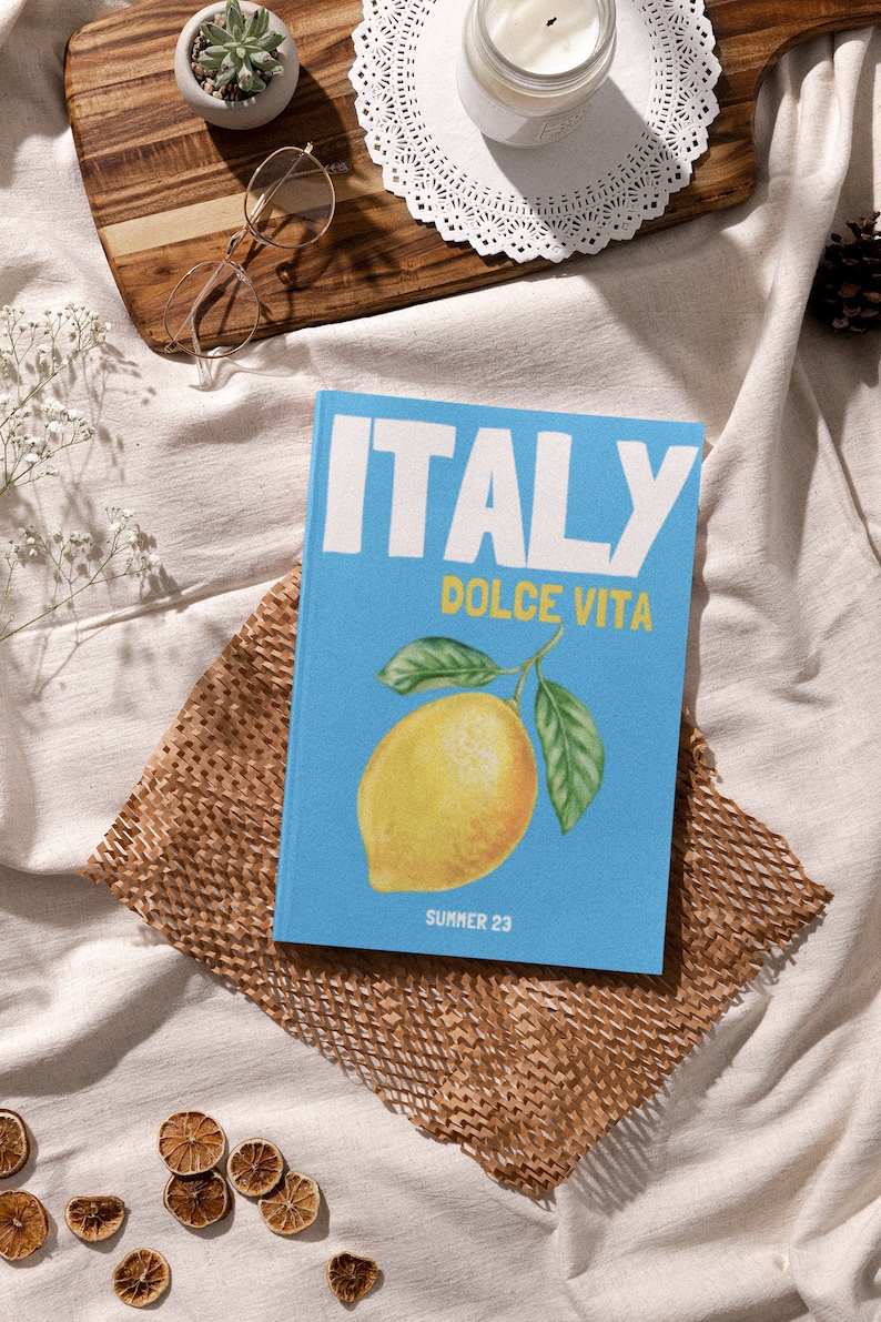 Puede incluir: Un libro azul con el texto "ITALY DOLCE VITA" y una ilustraci&oacute;n de lim&oacute;n. El texto "SUMMER 23" est&aacute; en la parte inferior del libro.