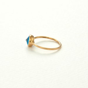 May include: A gold ring with a blue evil eye charm. The ring is a simple band with a small, round charm in the center.