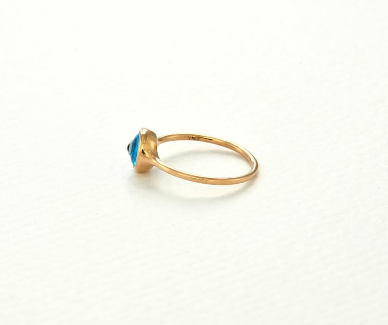 May include: A gold ring with a blue evil eye charm. The ring is a simple band with a small, round charm in the center.