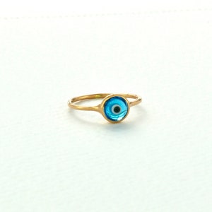 May include: A gold ring with a blue evil eye charm. The ring is a popular symbol of protection and good luck.