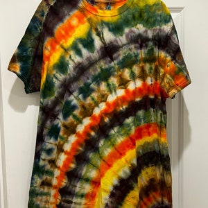 May include: A tie-dye t-shirt with a swirling pattern of orange, yellow, green, and brown colors.