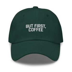 Puede incluir: Una gorra de béisbol verde oscuro con el texto "BUT FIRST, COFFEE" bordado en blanco en la parte delantera.