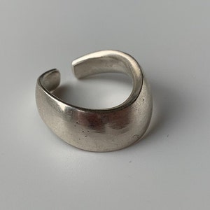 May include: A silver ring with a smooth, rounded surface. The ring is made of metal and has a simple, modern design.