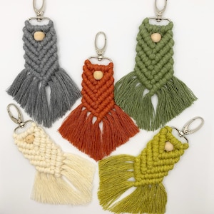 May include: Five colourful macrame keychains with wooden beads. Each keychain features a different colour and pattern, including grey, green, orange, white and yellow.