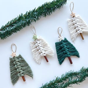Può includere: Quattro addobbi per l'albero di Natale in macramè fatti a mano. Due sono verdi e due sono bianchi. Ogni addobbo ha una piccola stella di legno in cima e un piolo di legno in fondo.
