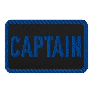 Könnte beinhalten: Ein rechteckiger, bestickter Aufnäher mit schwarzem Hintergrund und blauem Rand. Das Wort CAPTAIN ist in fetten, blauen, serifenlosen Großbuchstaben in der Mitte des Aufnähers eingestickt und weist eine strukturierte Garnoptik auf.