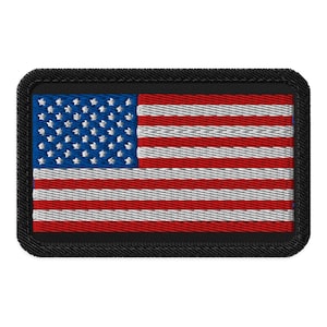 May include: A rectangular embroidered patch featuring the United States flag with a blue canton containing white stars and alternating red and white horizontal stripes. The entire design is bordered by a thick, solid black stitched edge.