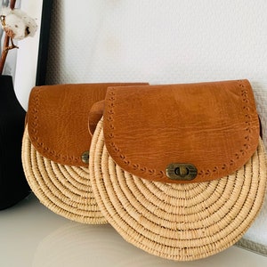 May include: Two round straw bags with brown leather flaps and a metal clasp. The bags have a woven design and are perfect for summer.