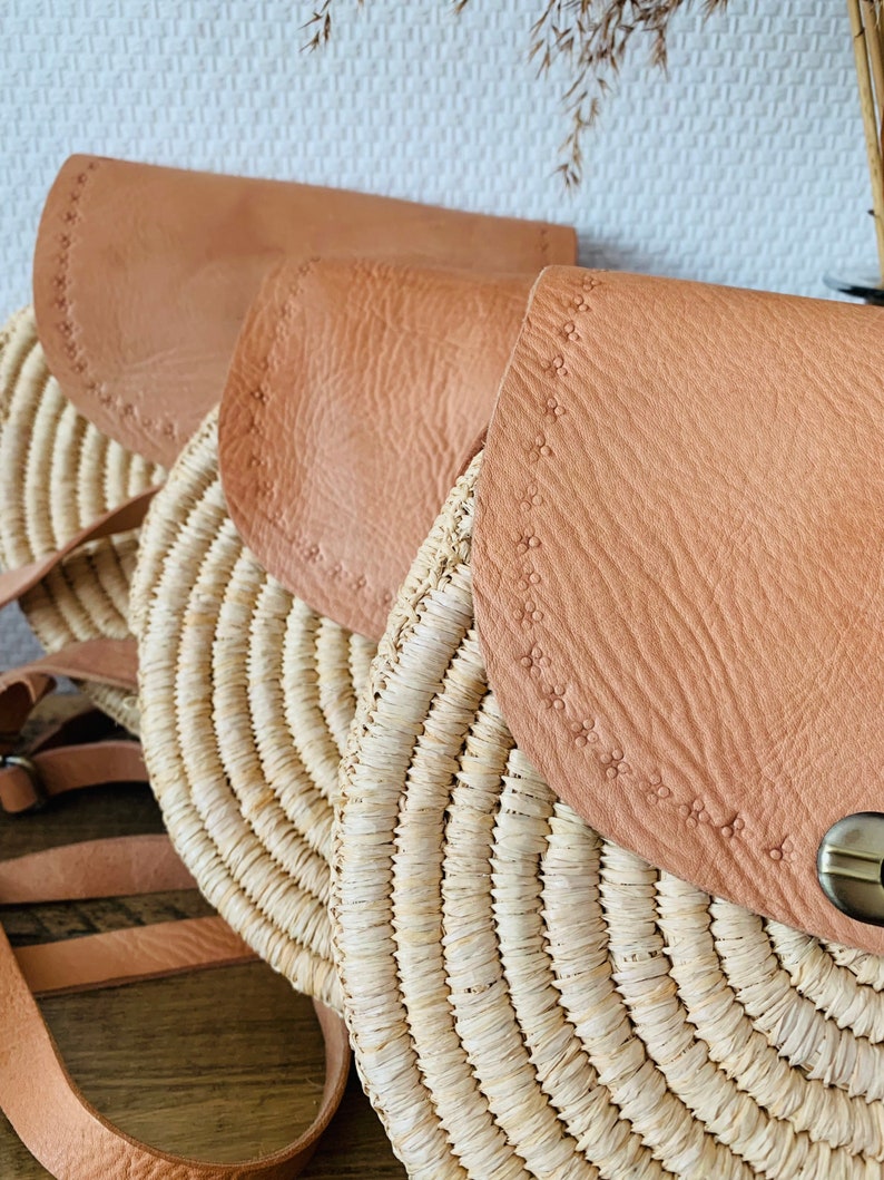 May include: Three round straw bags with brown leather flaps. The bags have a woven design and are lined with a decorative stitch.