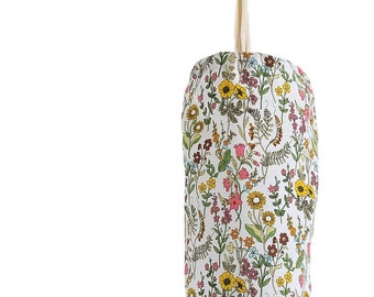 May include: A white fabric bag with a floral pattern in shades of yellow, pink, and green. The bag is hanging from a hook and is designed to hold grocery bags.