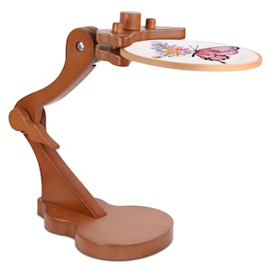 May include: A wooden embroidery stand with a butterfly design. The stand is made of light brown wood and features an adjustable arm and a round hoop holding the embroidered fabric. The embroidery hoop displays a pink butterfly and colorful flowers.