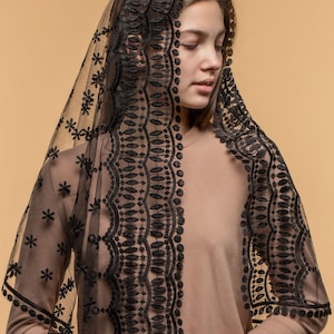 May include: A black lace veil with floral and geometric patterns. The veil is draped over the head and shoulders, creating a delicate and elegant look. The intricate lace design adds a touch of sophistication. The veil is a traditional accessory.
