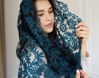 May include: A teal lace head covering with a floral design. The intricate lace drapes over the head and shoulders, creating a delicate and elegant look. The head covering is a deep teal color.
