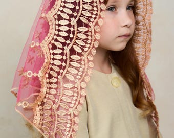 May include: A pink and burgundy veil with detailed lace edging. The veil is worn over a person's head, showing their face and a beige coat. The lace is a light peach colour, adding a delicate touch. The veil's design is elegant and refined.