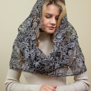 May include: A woman wearing a white sweater and blue jeans with a black lace shawl over her head.