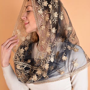 May include: Black and gold floral embroidered veil. The sheer fabric features an intricate gold floral pattern and a delicate lace trim. The veil is draped over the shoulders.