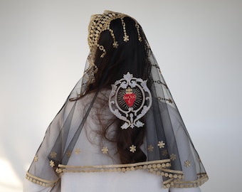 May include: Black veil with gold floral embroidery and trim. The veil features a decorative emblem with a red heart and crown design. The head covering is worn over dark hair.