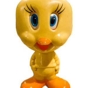 May include: A yellow plastic toy of Tweety Bird, a cartoon character from Looney Tunes. The toy has large blue eyes, a yellow beak, and orange feet.