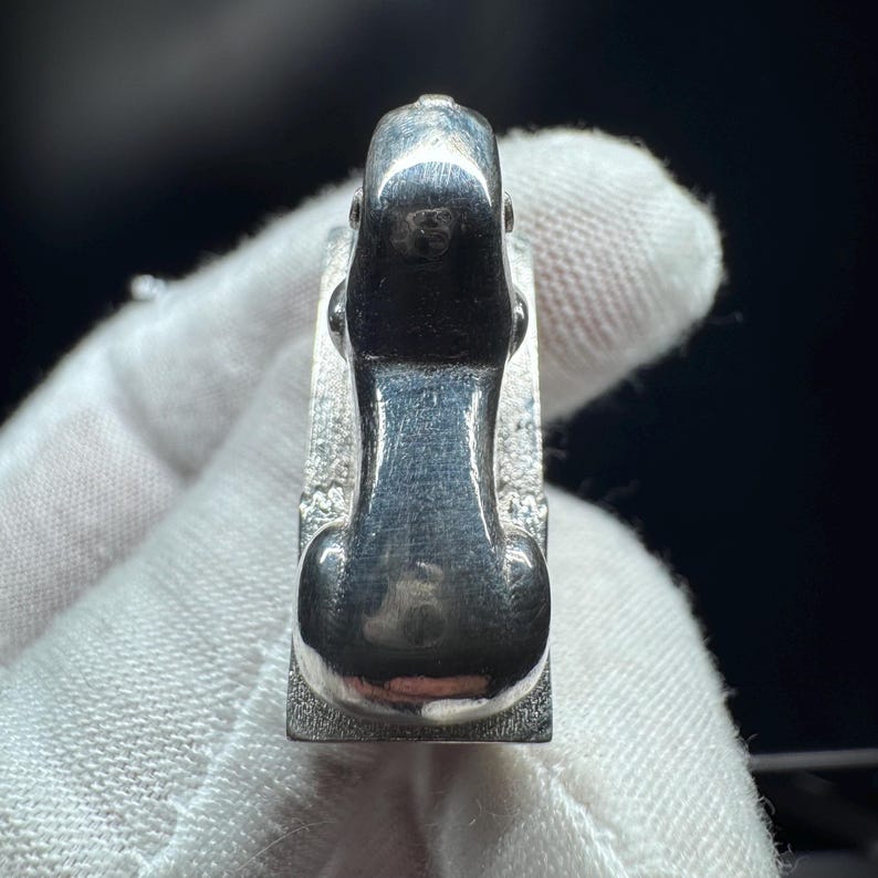 May include: A silver ring featuring a dog design. The dog is shown seated, with its head and body forming the ring's main feature. The ring has a rectangular base and a polished finish. The ring is likely made of sterling silver.