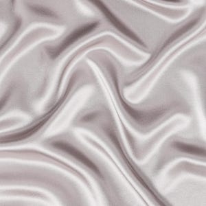 May include: A smooth, light mauve fabric with a lustrous, reflective surface. The material is draped in soft, flowing folds that create deep shadows and bright highlights across the surface, emphasizing the silky texture and consistent color.