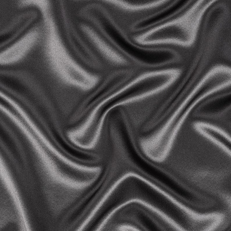 May include: A piece of dark charcoal gray fabric with a smooth, lustrous finish. The material is draped in soft, flowing folds that create deep shadows and bright highlights across the surface, emphasizing the reflective quality of the textile.