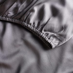 Peut inclure: Gros plan sur un drap-housse gris avec une texture lisse et soyeuse. Le drap est fait d'un tissu doux et luxueux.