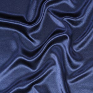May include: A deep navy blue fabric with a smooth, lustrous finish. The material features soft, flowing folds and ripples that create a dynamic play of light and shadow across the surface, highlighting the reflective quality of the textile.