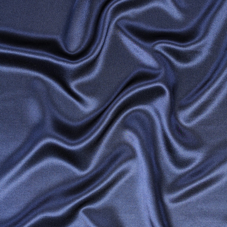May include: A deep navy blue fabric with a smooth, lustrous finish. The material features soft, flowing folds and ripples that create a dynamic play of light and shadow across the surface, highlighting the reflective quality of the textile.