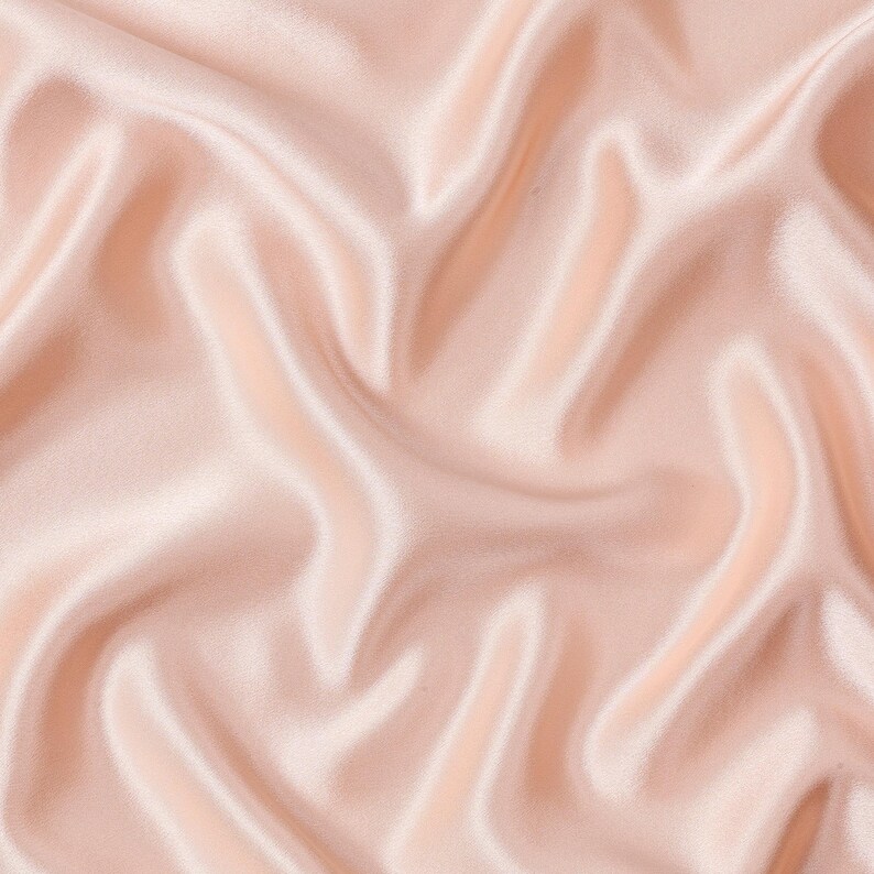 May include: A light blush pink fabric with a smooth, lustrous surface and a soft sheen. The material is draped in deep, flowing folds that create a series of highlights and shadows across the surface, emphasizing the fluid texture of the textile.