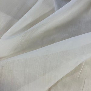 Puede incluir: Primer plano de una tela blanca transparente con una textura suave. La tela está doblada y drapeada, creando pliegues y arrugas suaves.