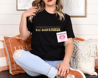 以下が含まれることがあります： 金色の文字で「Overstimulated 911 Dispatcher」と書かれた黒いTシャツ。 ソファに座って白とオレンジのクッションのある人に着られています。