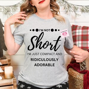 May include: Gray t-shirt with black text that reads "...I'm not... short I'm just compact and ridiculously adorable".