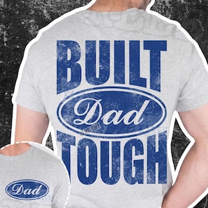 Könnte beinhalten: Ein hellgraues T-Shirt mit einer großen blauen Grafik auf der Rückseite mit dem Text BUILT DAD TOUGH in einer abgenutzten Schriftart, wobei das Wort Dad in einem Oval steht. Eine kleinere Version der blauen ovalen Dad-Grafik ist vorne aufgedruckt.