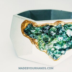 May include: A white hexagonal concrete planter with a gold rim and a design of green and blue crystals embedded in the side.
