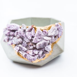May include: A small, geometric concrete planter with a light gray finish. The planter is decorated with a band of purple and gold crystals.